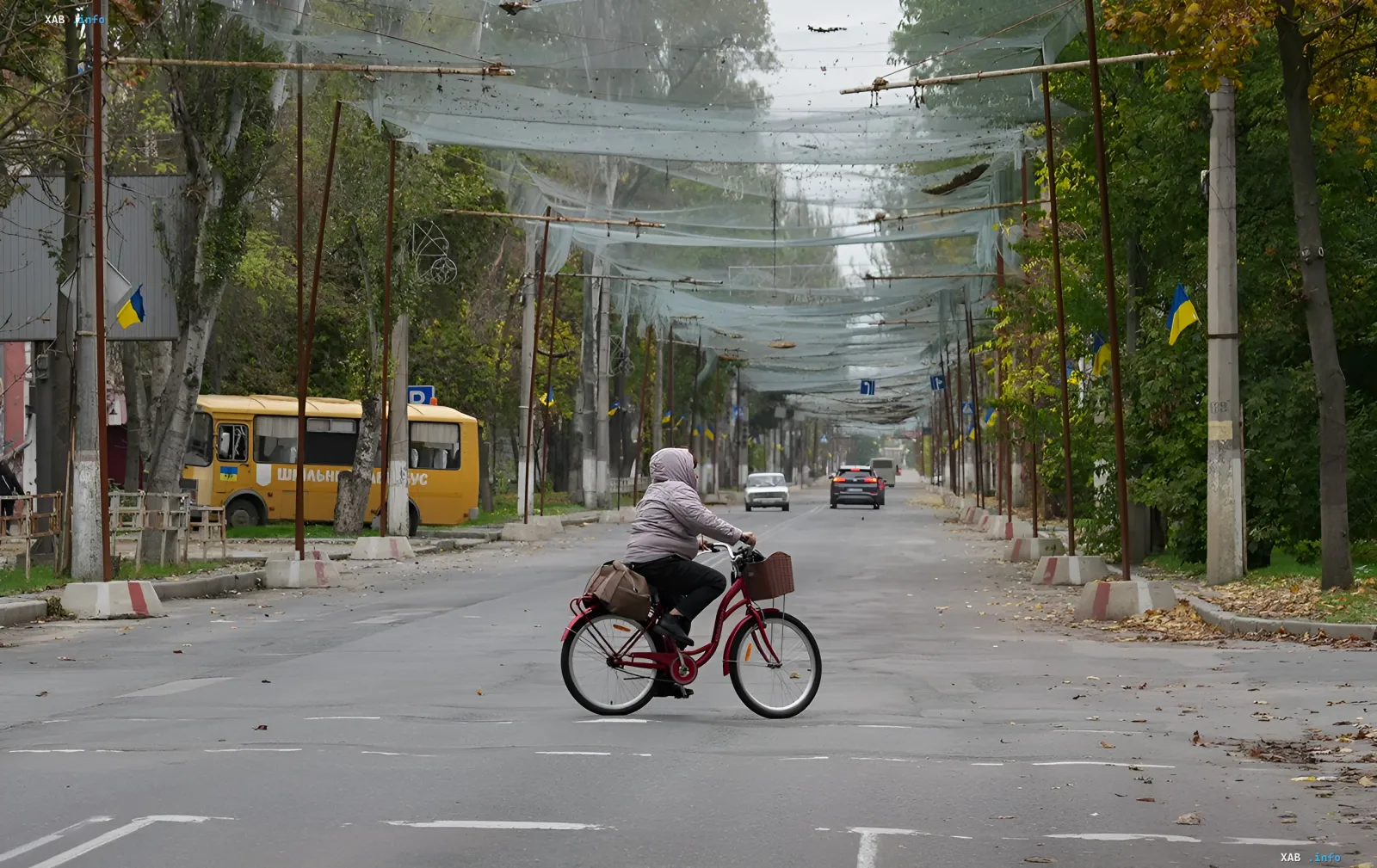 Eine Frau fährt mit dem Fahrrad auf einer leeren Straße einer ukrainischen Stadt mit Tarnnetzen über der Straße