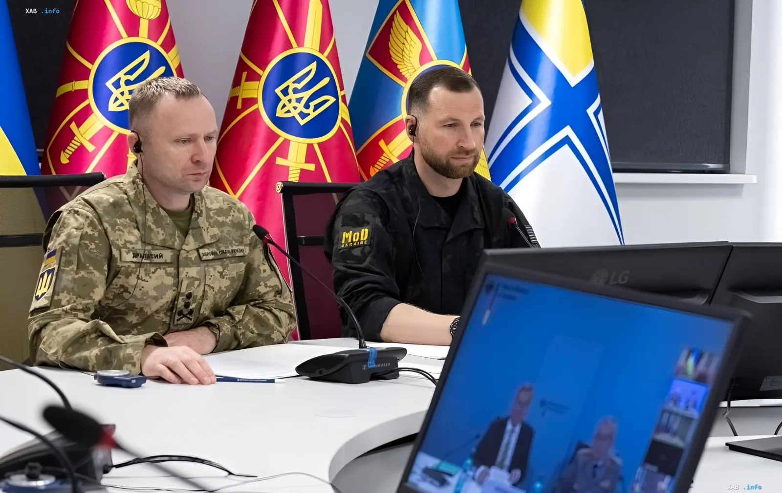 Украинские военные чиновники в камуфляже сидят за столом на фоне флагов во время онлайн-конференции