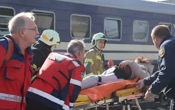 Спасатели и медики оказывают помощь пострадавшей на носилках возле поврежденного поезда