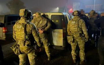 Militärpersonal in Camouflage-Uniformen mit DBR-Kennzeichnungen führt nachts eine Spezialeinsatzoperation zur Festnahme einer Person an einem weißen Kleinbus durch