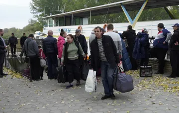 Eine Gruppe evakuierter Bewohner mit Koffern und Taschen bereitet sich am Pier auf das Besteigen eines Schiffes vor