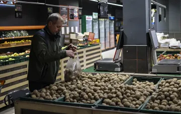 Пожилой покупатель выбирает и упаковывает картофель в пластиковый пакет в супермаркете