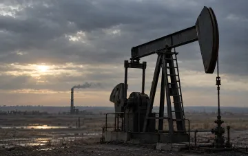 Нефтяная качалка на фоне промышленного завода и заката в пасмурный день