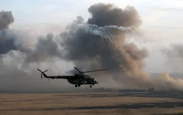 Военный вертолет Ми-8 совершает полет над открытой местностью на фоне густого дыма после удара дрона