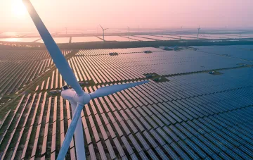 Windkraftanlage vor einer riesigen Solarpark-Fläche bei Sonnenuntergang