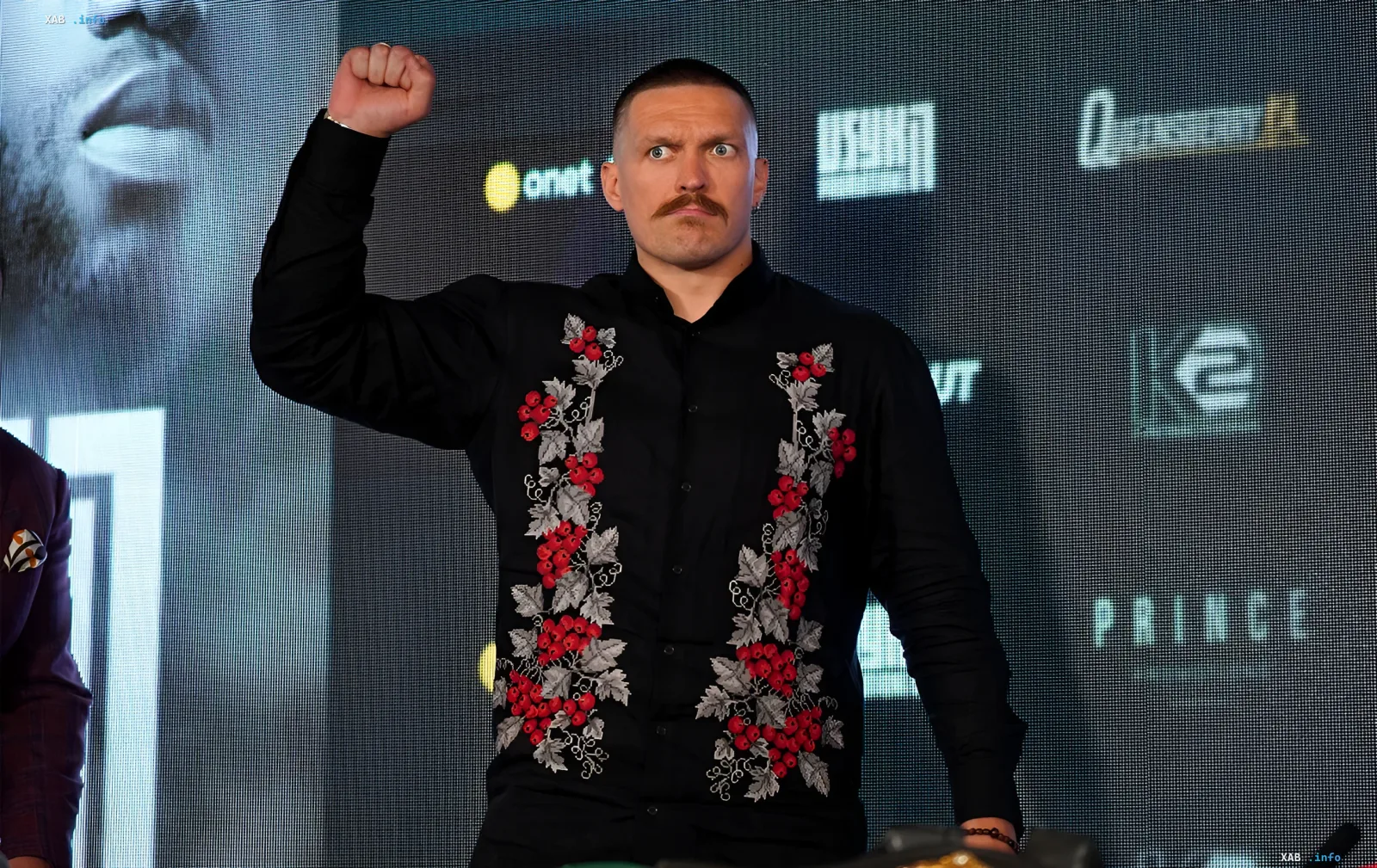 Украинский боксер Александр Усик в черной вышиванке поднимает кулак на пресс-конференции