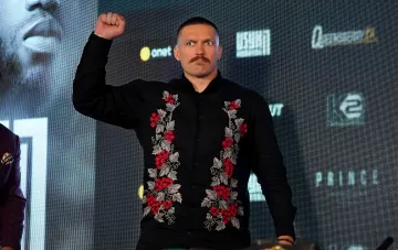 Украинский боксер Александр Усик в черной вышиванке поднимает кулак на пресс-конференции