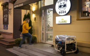 Женщина в желтой куртке идет мимо магазина Coffee Boss, рядом с которым установлен электрогенератор