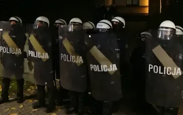 Экипированные сотрудники польской полиции в защитном снаряжении стоят с щитами ночью.