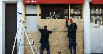 Рабочие заколачивают витрину магазина деревянными щитами перед протестами на Хэллоуин во Франции