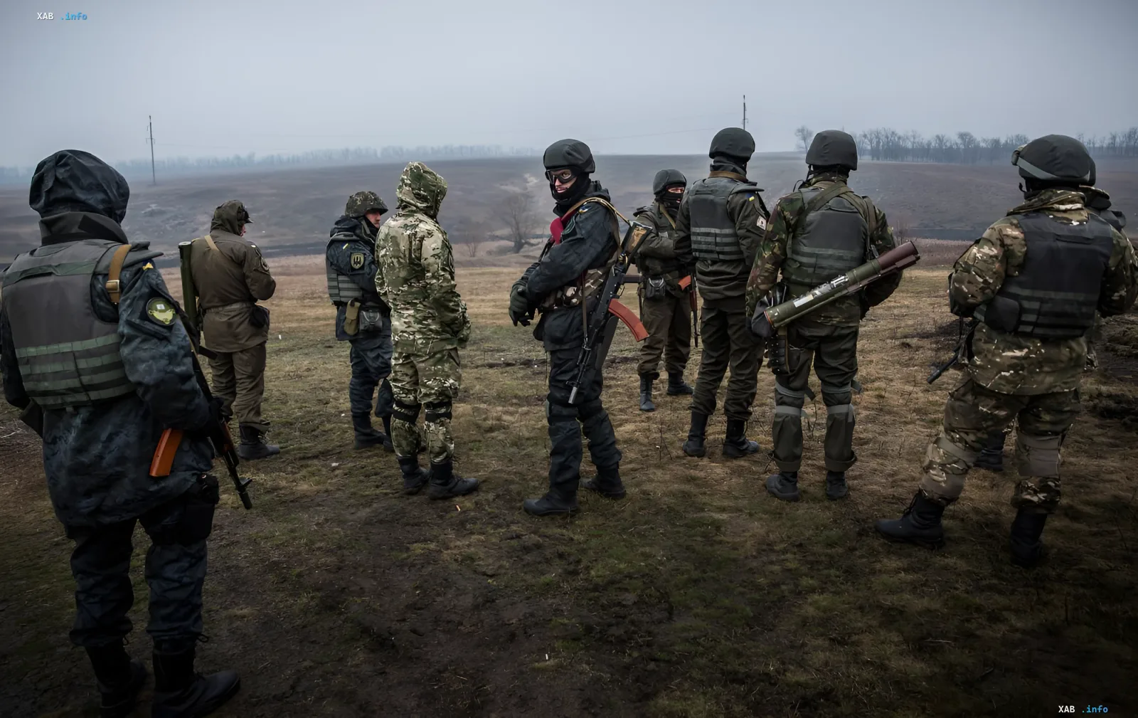 Armed Ukrainian servicemen in camouflage uniforms and helmets stand against an open landscape background