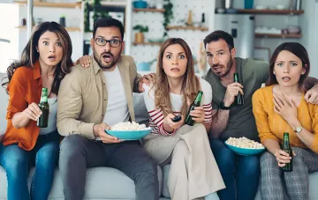 Freunde mit Bier und Popcorn auf dem Sofa schauen ängstlich beim Horrorfilm zu