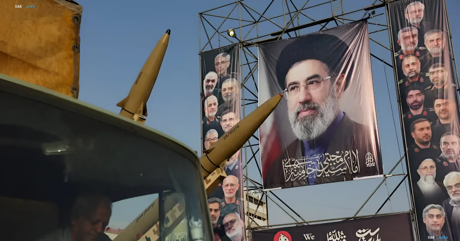 Military missiles on a truck in front of huge banners with portraits of Iranian leaders and military commanders outdoors
