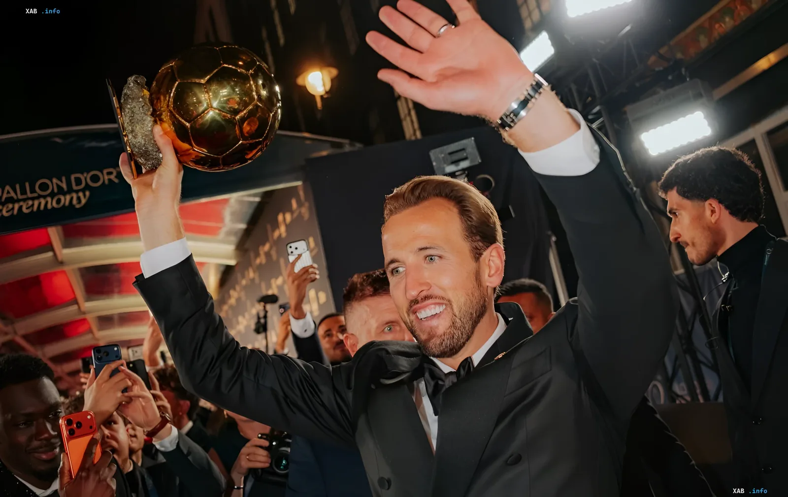 Harry Kane holding the Ballon d'Or trophy high and waving at the awards ceremony